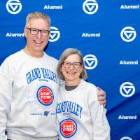 Couple smiling at camera in front of GV Alumni backdrop wearing crewnecks